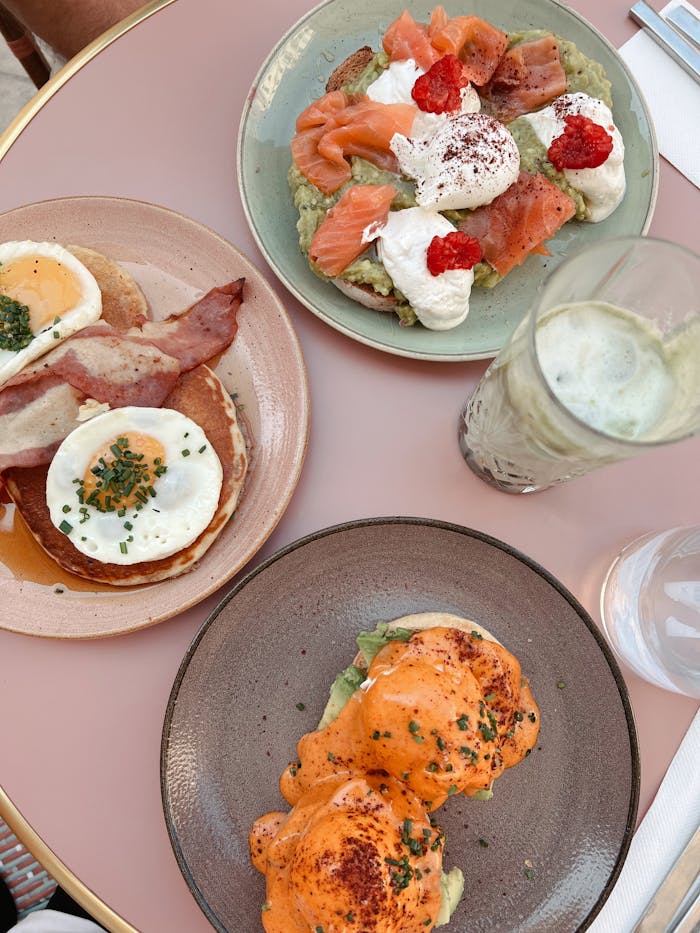 Delicious brunch with avocado toast, salmon, eggs, and drinks on a pastel table.