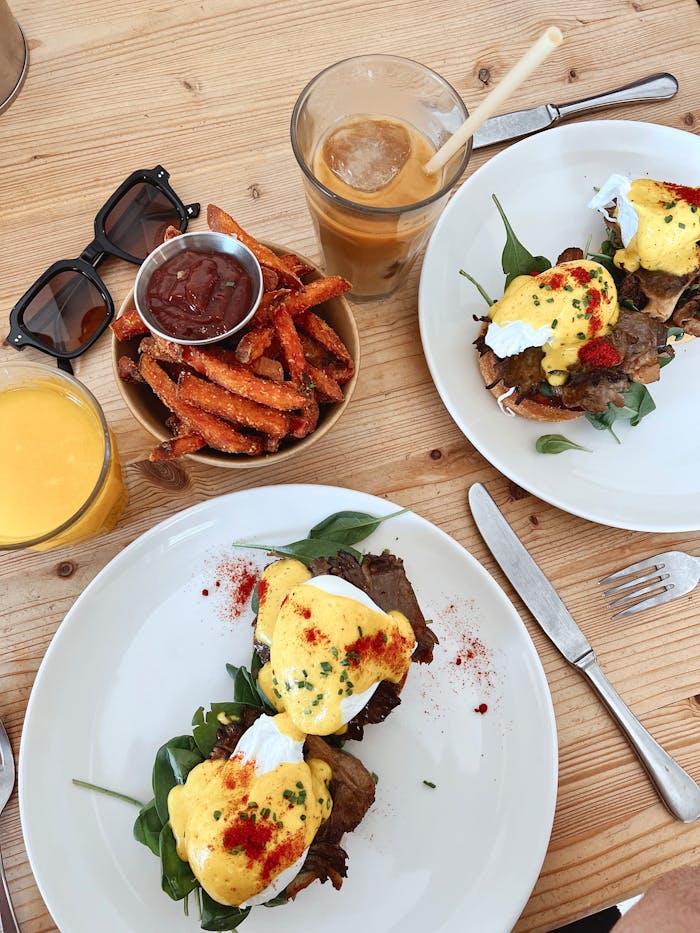 Top view of a brunch table featuring Eggs Benedict and sweet potato fries.